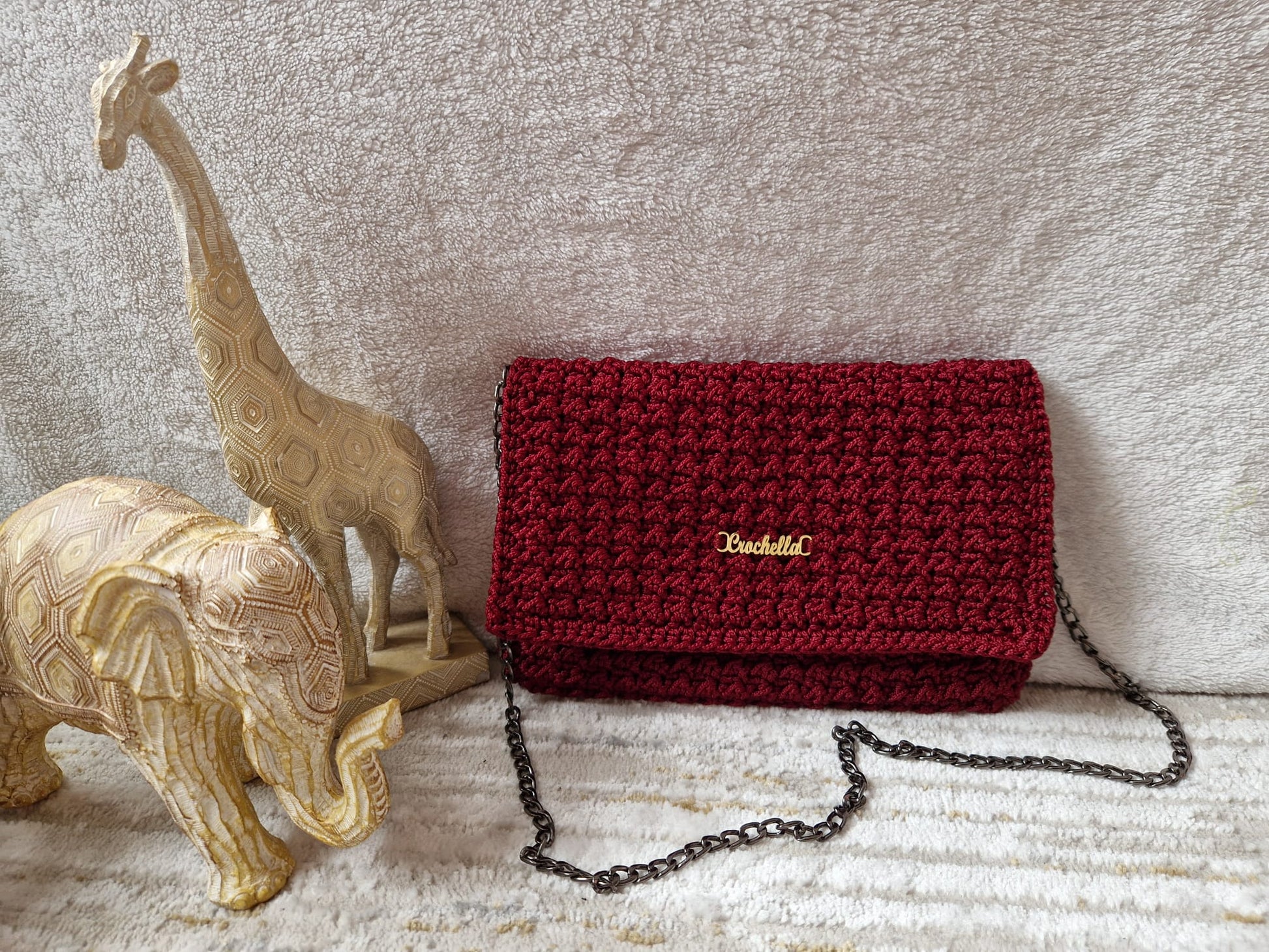 Crimson Luxe Crochet Clutch displayed beside carved giraffe and elephant figurines, highlighting its deep red hue and gold Crochella logo.