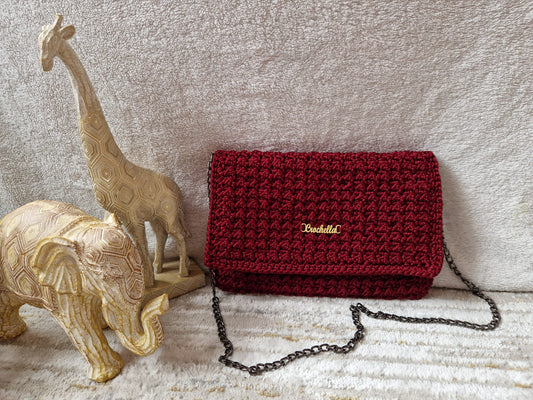 Crimson Luxe Crochet Clutch displayed beside carved giraffe and elephant figurines, highlighting its deep red hue and gold Crochella logo.