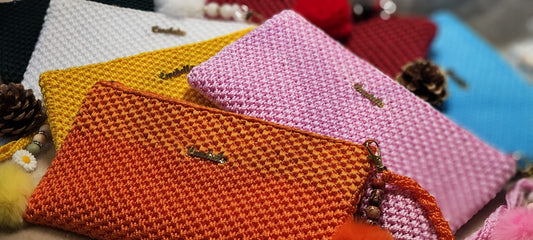 All seven Crochella Luxe Clutches arranged in a fan layout on a soft beige blanket, showcasing the full color range.