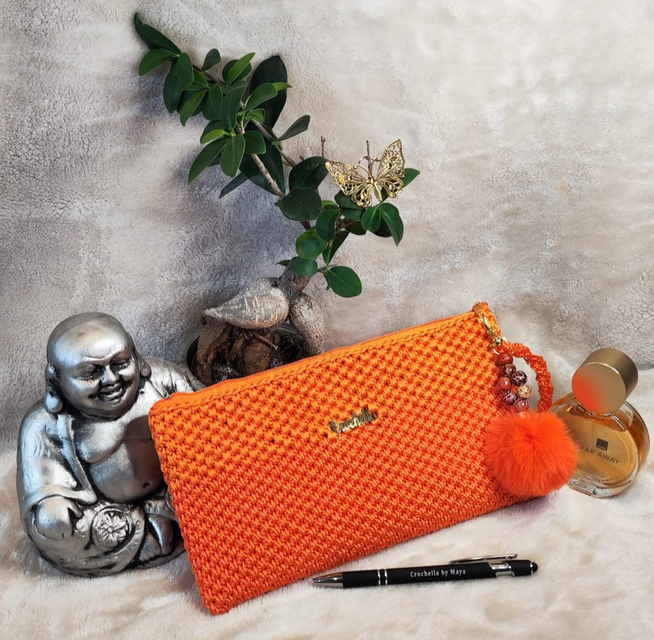 Vibrant orange Crochella Luxe Clutch with pom-pom charm, perfect for bold style.