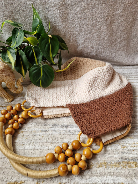Earthy Boho Crochet Shoulder Bag in cream and brown tones with chunky wooden bead handles, styled next to a leafy plant on a neutral background.