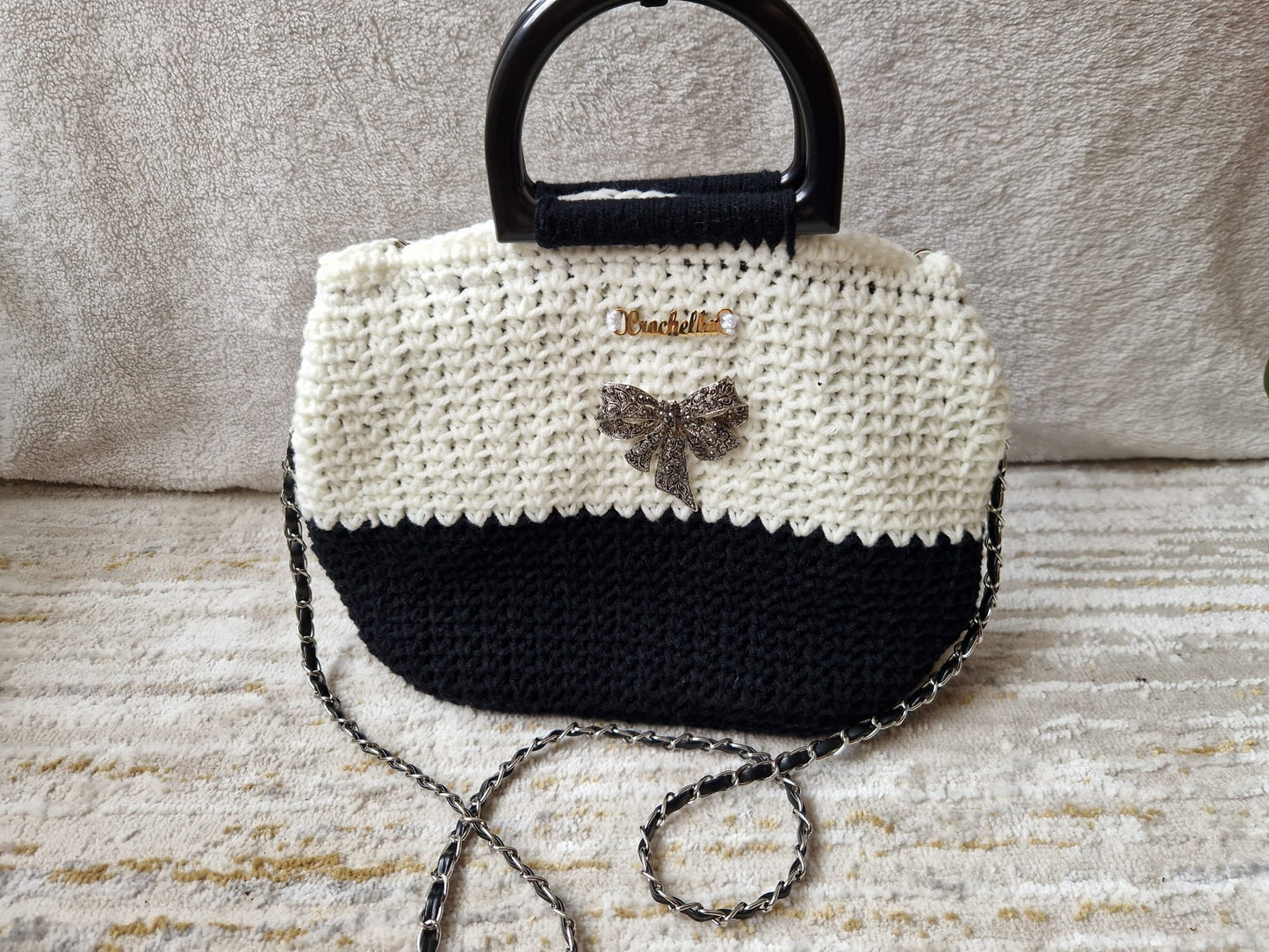 Elegance Bow Crochet Handbag in black and white with a sparkling bow brooch and a chain strap, featuring a structured handle and gold Crochella logo.