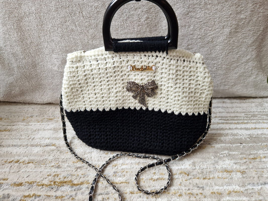 Elegance Bow Crochet Handbag in black and white with a sparkling bow brooch and a chain strap, featuring a structured handle and gold Crochella logo.