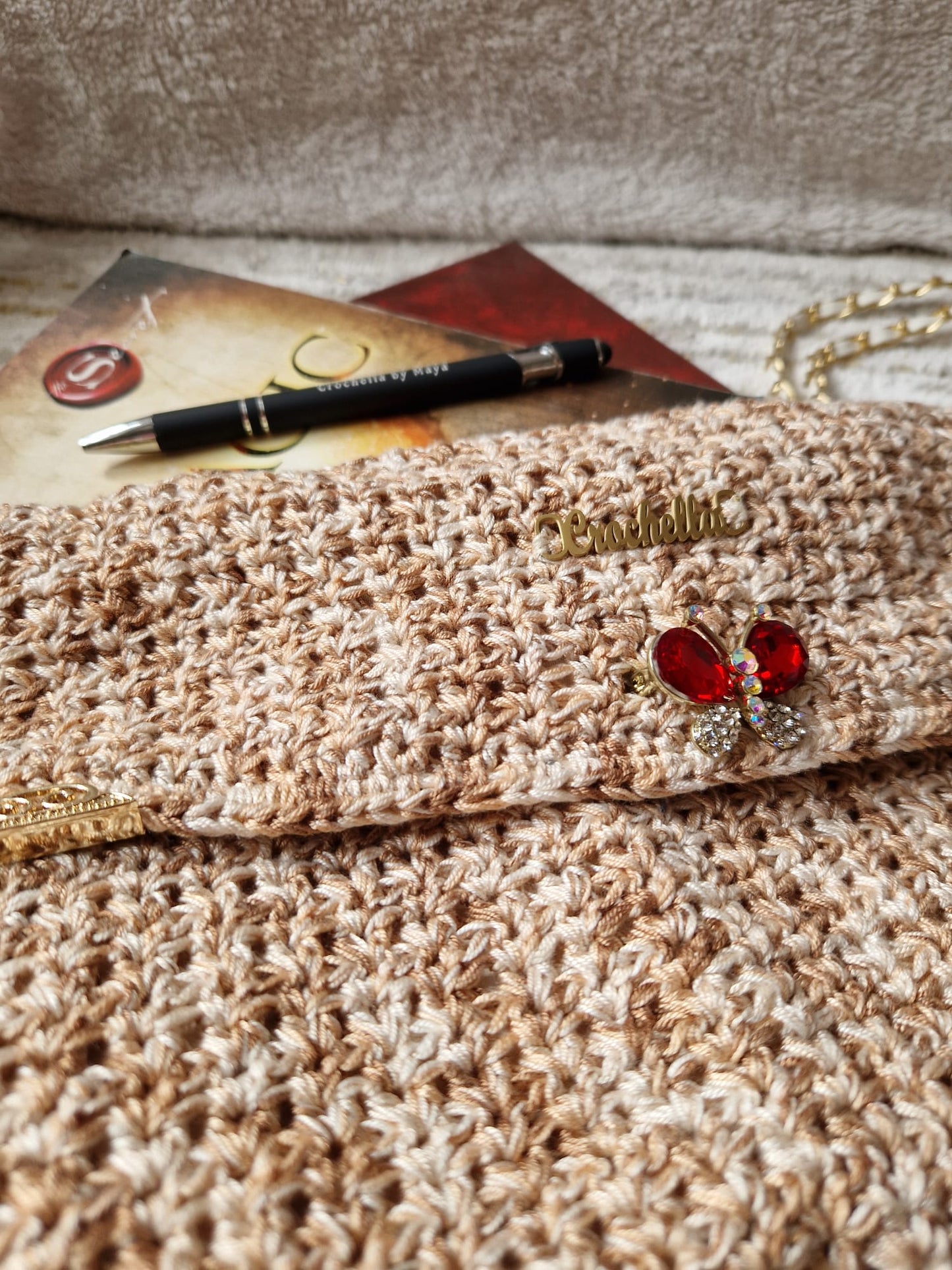Close-up of the Golden Elegance Clutch's butterfly clasp, gold-trimmed edges, and soft crochet stitching.