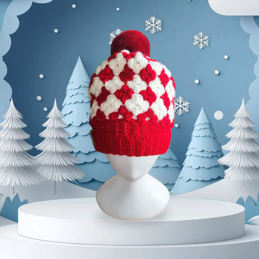 Handmade red and white crochet beanie styled on a mannequin, featuring classic granny square pattern and fluffy pom-pom.