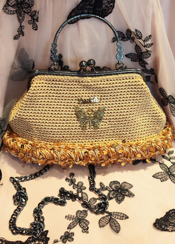 Golden Glow handbag from the Royal Bloom Collection, featuring a metallic butterfly emblem and textured loop trim.