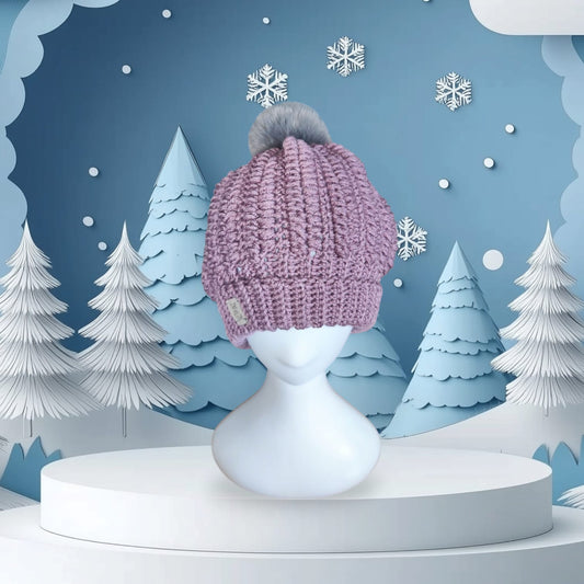 Soft Lavender handmade crochet beanie with gray faux-fur pom-pom, displayed on a mannequin with a winter-themed backdrop.