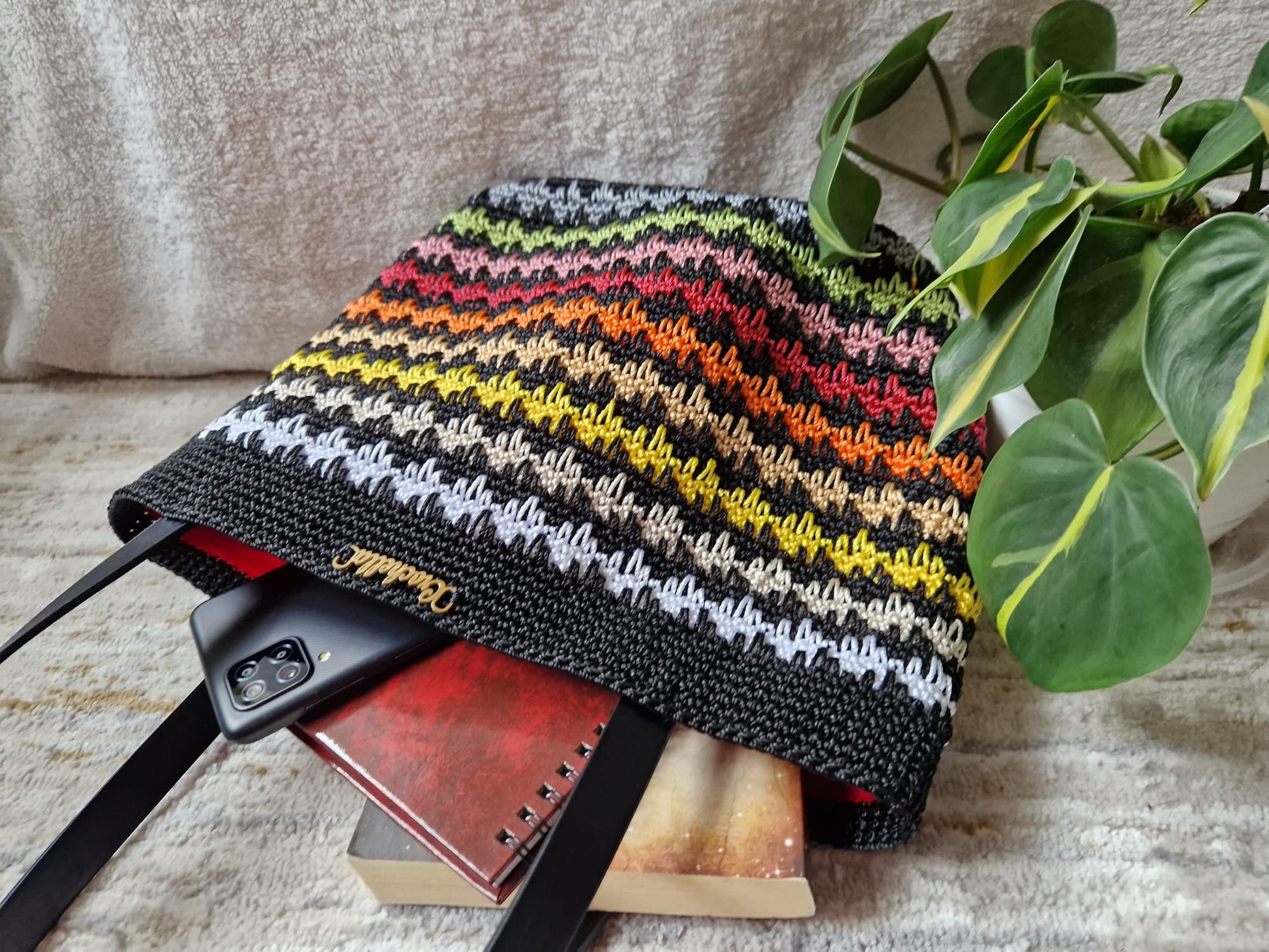 Sunset Stripes Crochet Tote displayed on a pedestal with Crochella branding, featuring warm gradient rows in yellow, orange, and red.
