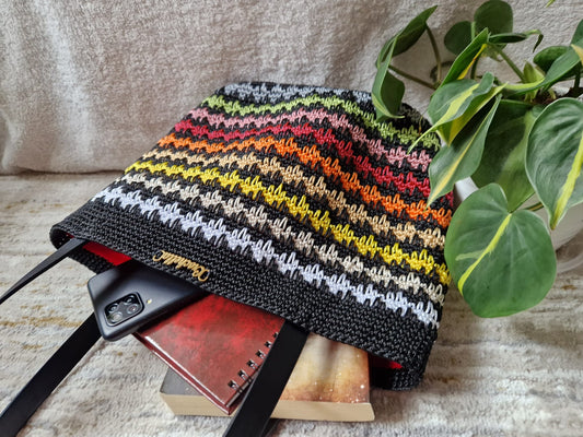 Sunset Stripes Crochet Tote displayed on a pedestal with Crochella branding, featuring warm gradient rows in yellow, orange, and red.