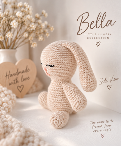 A crocheted bunny plush toy in a warm cream color, shown in a soft, styled setting with dried flowers, a wooden heart sign, and text overlays reading 'Bella', 'Little Lunéra Collection', and 'Side View'.