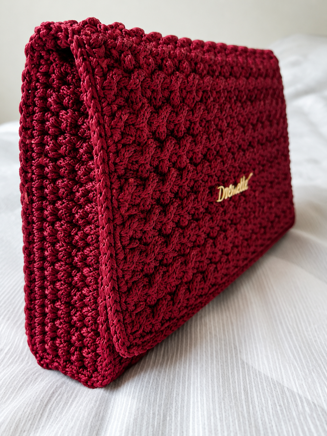 Red crochet clutch bag with crochella branding on a front of the bag