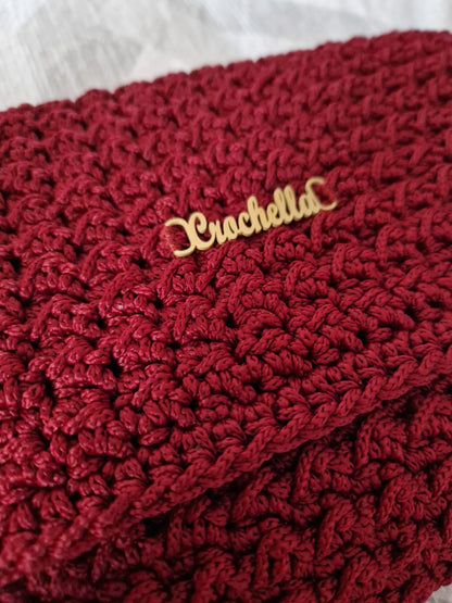 Close-up of the Crimson Luxe Clutch showcasing its rich crochet texture and signature gold logo detail.
