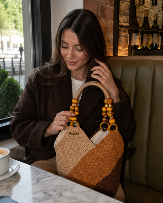 Woman holding a handmade brown and beige crochet handbag in a cozy café setting with warm elegant atmosphere