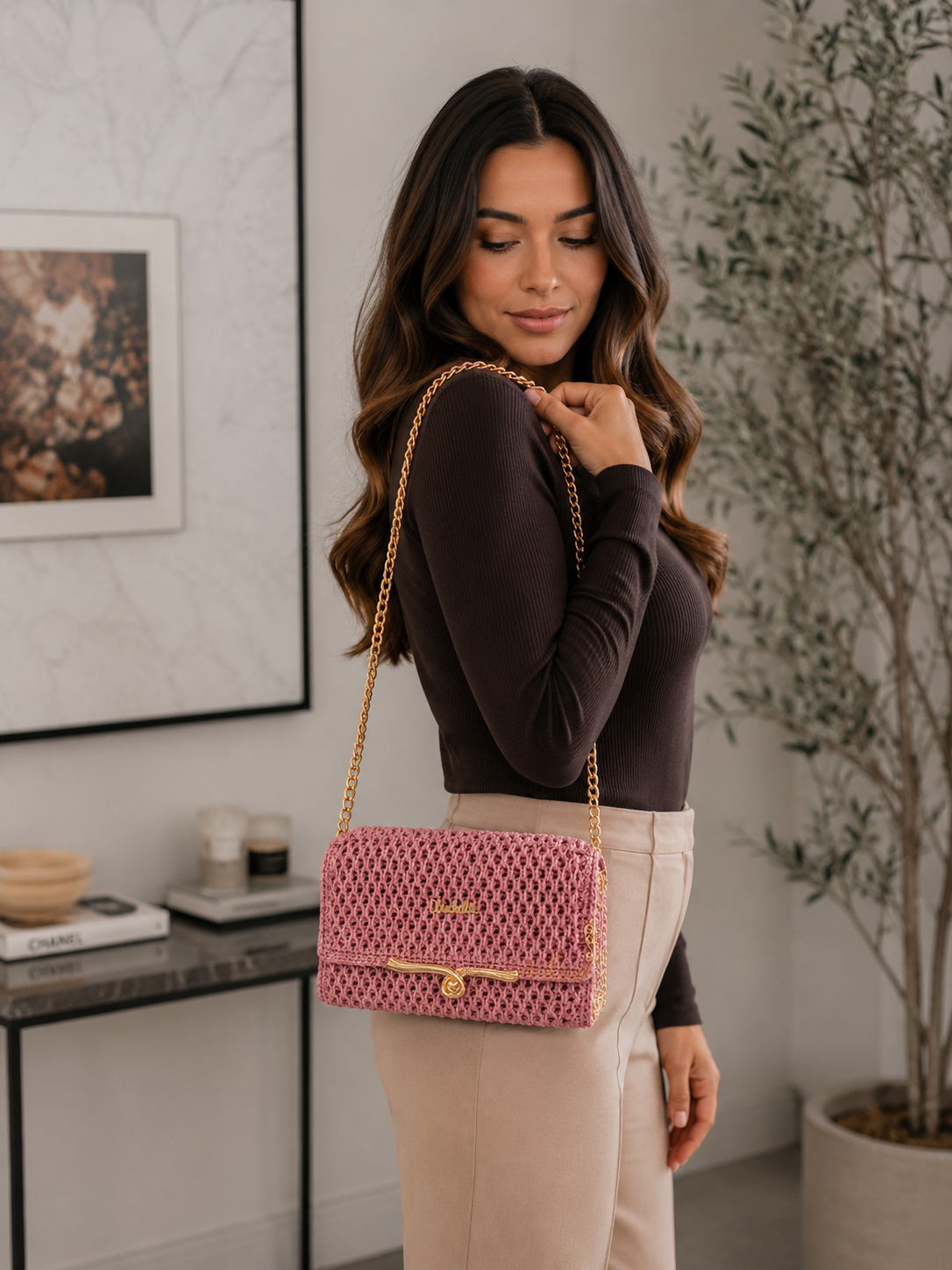 Woman holding a pink handbag with gold chain strap in an indoor setting