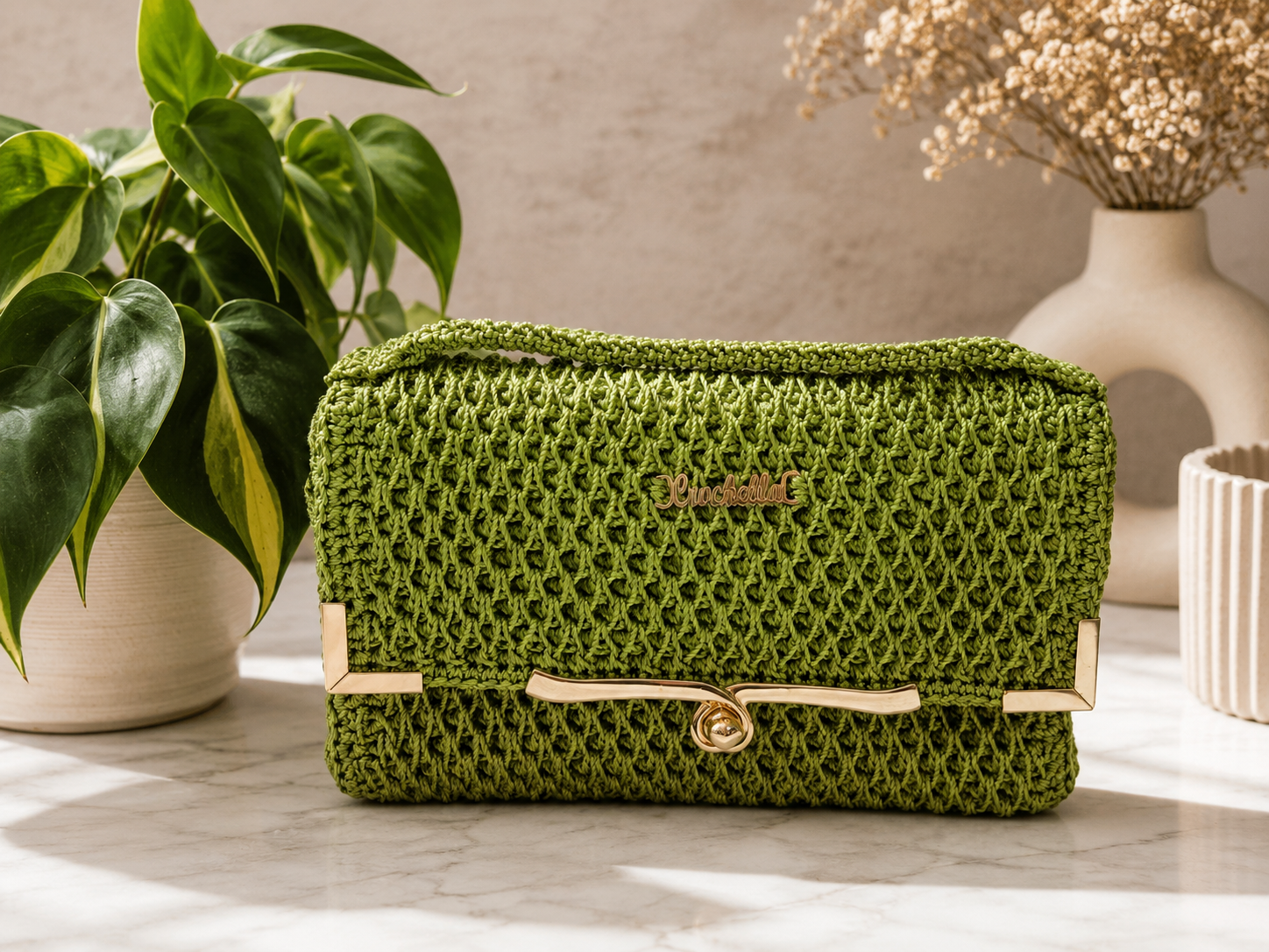 Green woven clutch bag on a marble surface with decorative plants and vases in the background