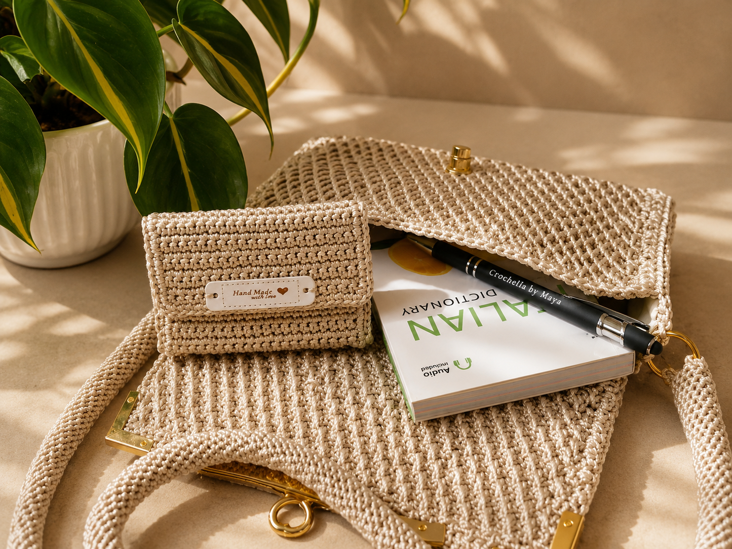 Beige woven handbag with a book and pen on a light surface, with a plant in the background.