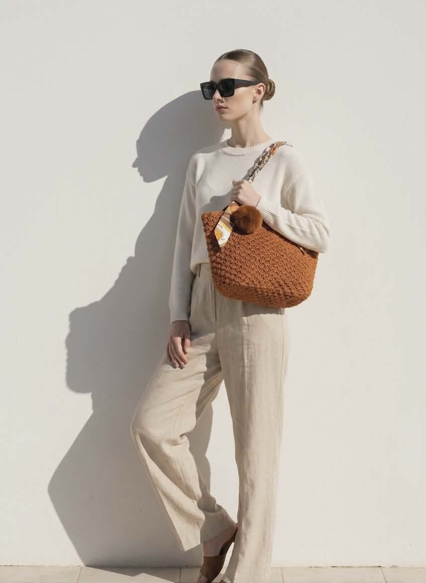 Woman holding a brown woven handbag against a white wall