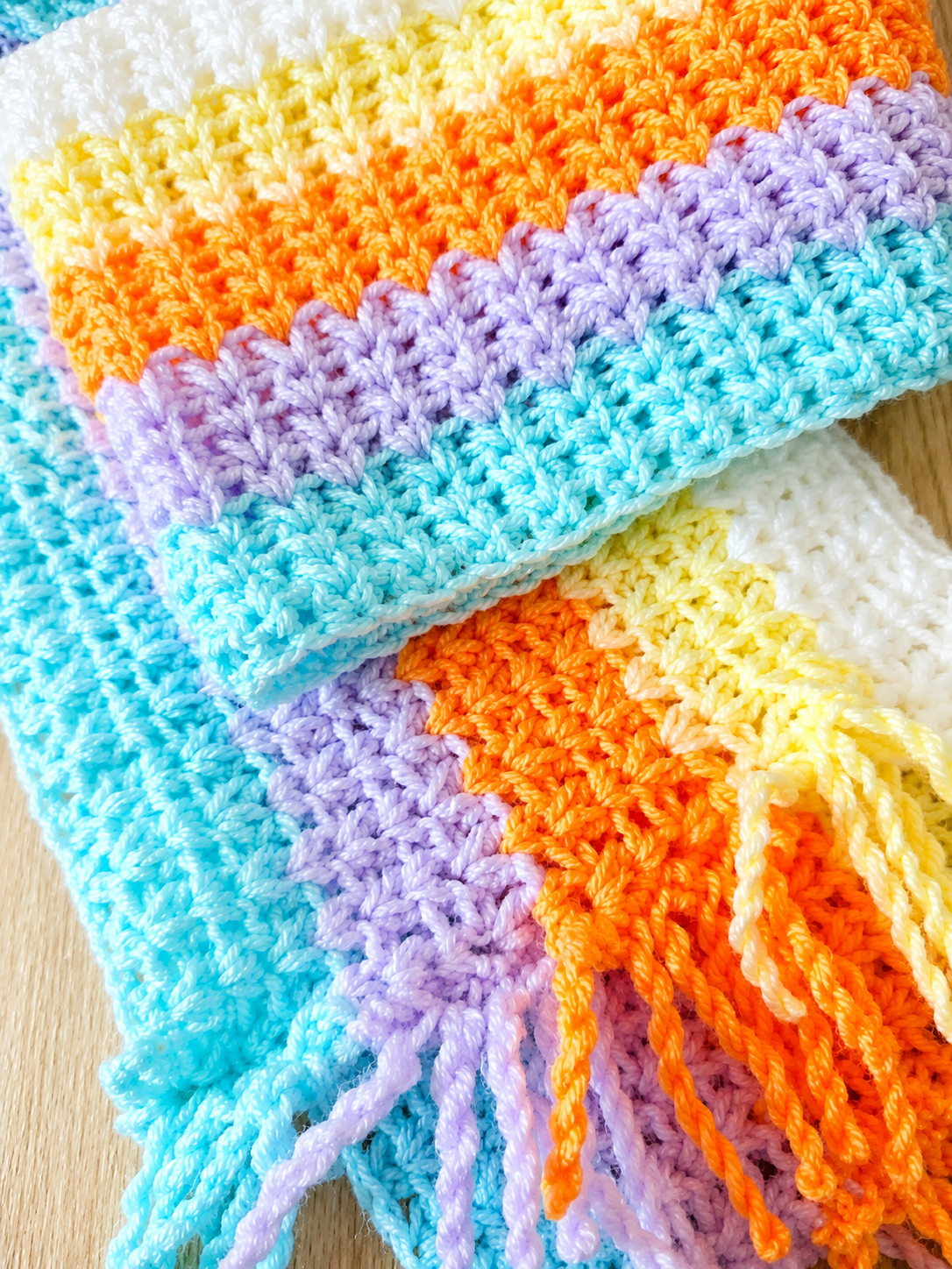Colorful crocheted blanket with a striped pattern on a wooden surface